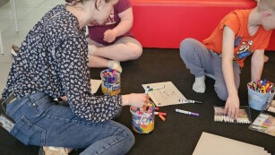 Uczniowie razem z pracownikiem biblioteki rysują kredkami na podłodze