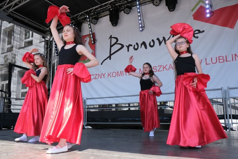 Tańczące dziewczynki w czerwonych spódnicach, w tle baner Bronowice