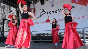 Tańczące dziewczynki w czerwonych spódnicach, w tle baner Bronowice