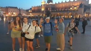 Grupa młodzieży z opiekunami pozuje do zdjęcia na tle krakowskich sukiennic