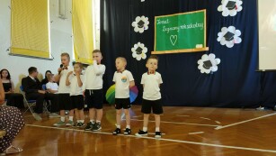 grupa dzieci z przedszkola stoi w sali gimnastycznej podczas występu z okazji zakończenia roku szkolnego